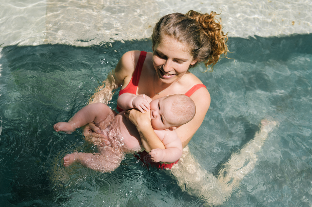 Young mom swimming with baby in water doing postpartum exercise