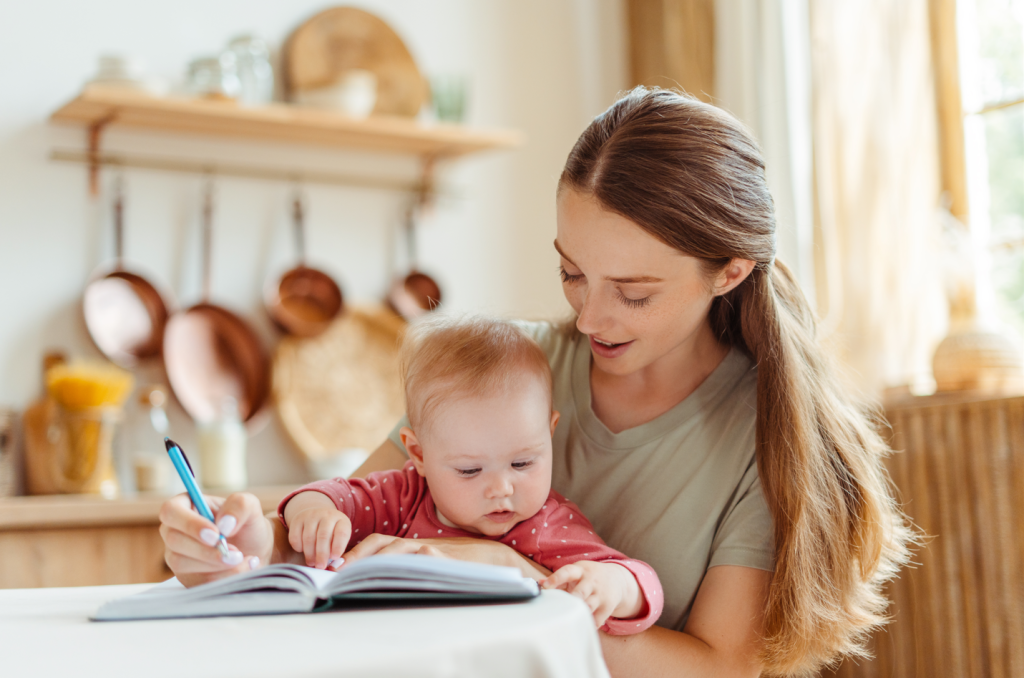 Mom writing in training log notebook with baby in arms