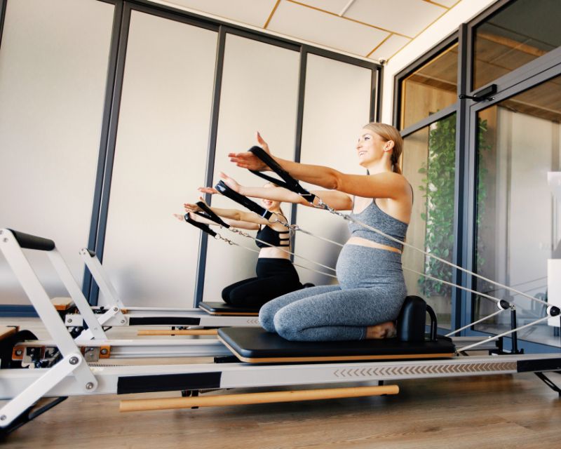 Happy postpartum moms attending a reformer Pilates class